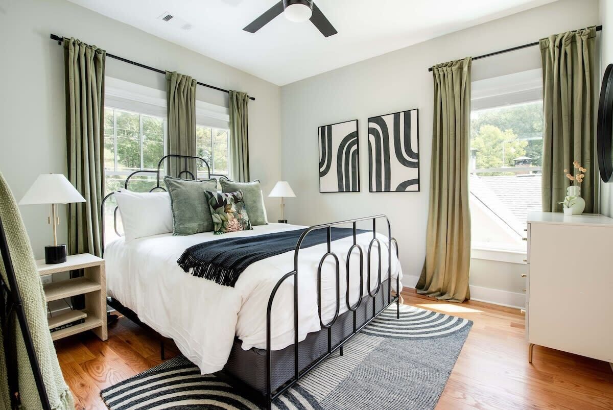 Une chambre à coucher comprenant un lit, des tables de chevet, un ventilateur de plafond et de grandes fenêtres avec des rideaux.