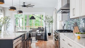 A modern kitchen with a central island, built-in appliances, and a large window offering a view of the outdoors. - Aquarius Rising (Atlanta)