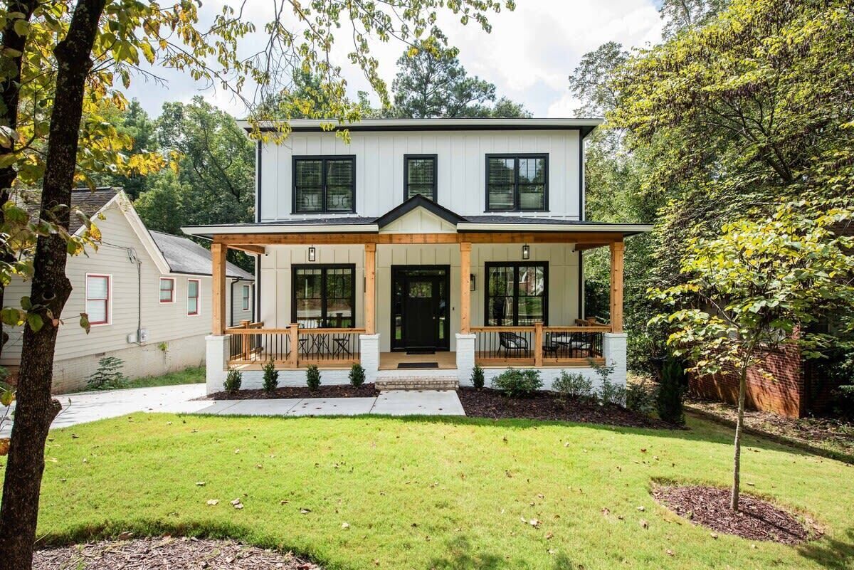 A two-story house with a front porch, a black front door, and a small front yard.