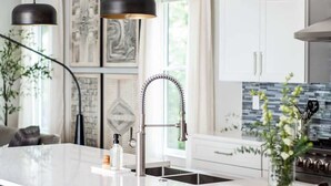 A modern kitchen with a large island, pendant lights, and a stainless steel faucet. - Aquarius Rising (Atlanta)