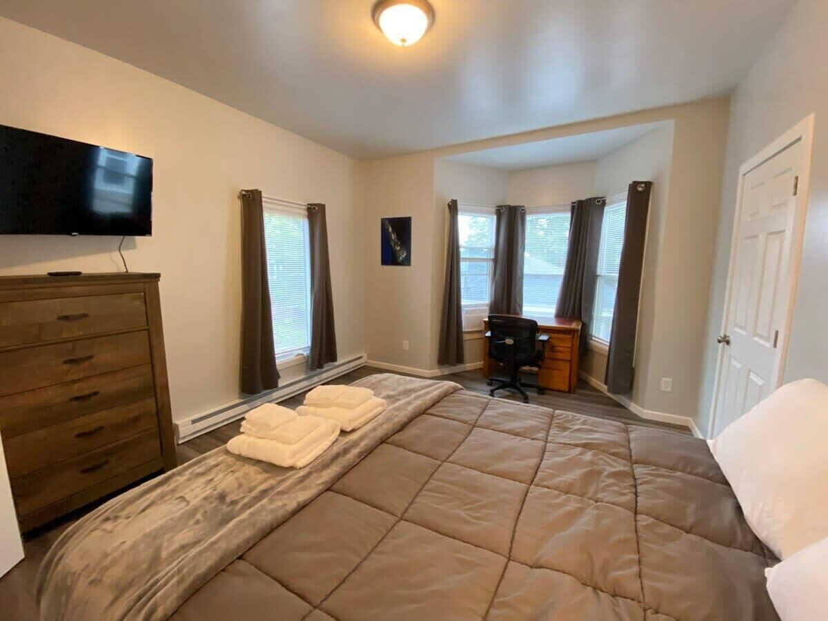 A bedroom with a large bed, a dresser, a desk, and a flat-screen TV.