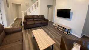 Ein modernes Wohnzimmer mit einem braunen Ledersofa, einem Holztisch und einem flachbildfernseher an der Wand.