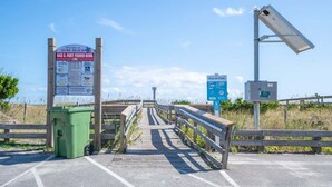 A wooden boardwalk leading to a beach area with a sign indicating '643 S. Fort Fisher Blvd.' and a 'Pay to Park' sign.
