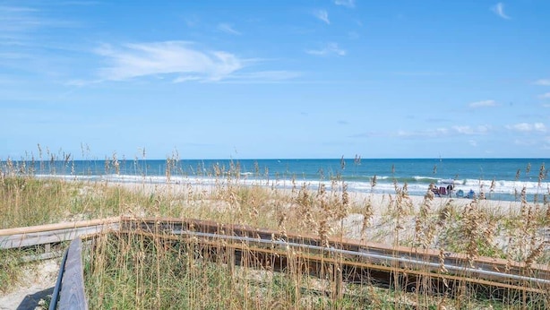 A beach view with a wooden boardwalk, beach grass, and the ocean.