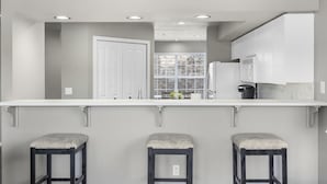 A kitchen with a white countertop, three stools, a window with a view, and a door. - Modern 2-Bed Condo with Golf Course Views in Branson (Branson)