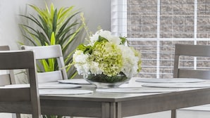 A dining table with a floral centerpiece, two chairs, and a window with blinds. - Modern 2-Bed Condo with Golf Course Views in Branson (Branson)