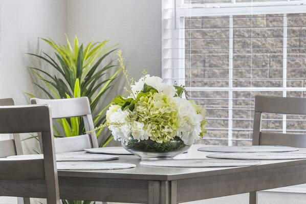 A dining table with a floral centerpiece, two chairs, and a window with blinds. - Modern 2-Bed Condo with Golf Course Views in Branson (Branson)