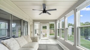 A covered porch with a ceiling fan, a beige couch, and large windows offering views of the backyard. - Modern 2-Bed Condo with Golf Course Views in Branson (Branson)