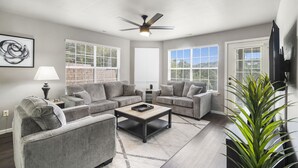 A modern living room with grey sofas, a coffee table, and a ceiling fan. - Modern 2-Bed Condo with Golf Course Views in Branson (Branson)