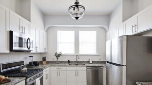A modern kitchen with white cabinets, stainless steel appliances, a granite countertop, and a patterned floor. - Beautiful 3 bedroom home w/Patio, BBQ Grill & Fire table. Steps from 7th Ave.  (Tampa)