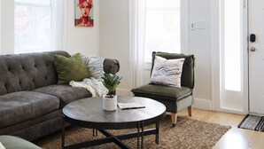 A modern living room with a ceiling fan, a grey sofa, a green armchair, and a coffee table. - Beautiful 3 bedroom home w/Patio, BBQ Grill & Fire table. Steps from 7th Ave.  (Tampa)