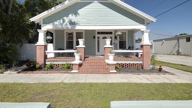 A two-story house with a front porch, brick columns, and a small garden. - Beautiful 3 bedroom home w/Patio, BBQ Grill & Fire table. Steps from 7th Ave.  (Tampa)