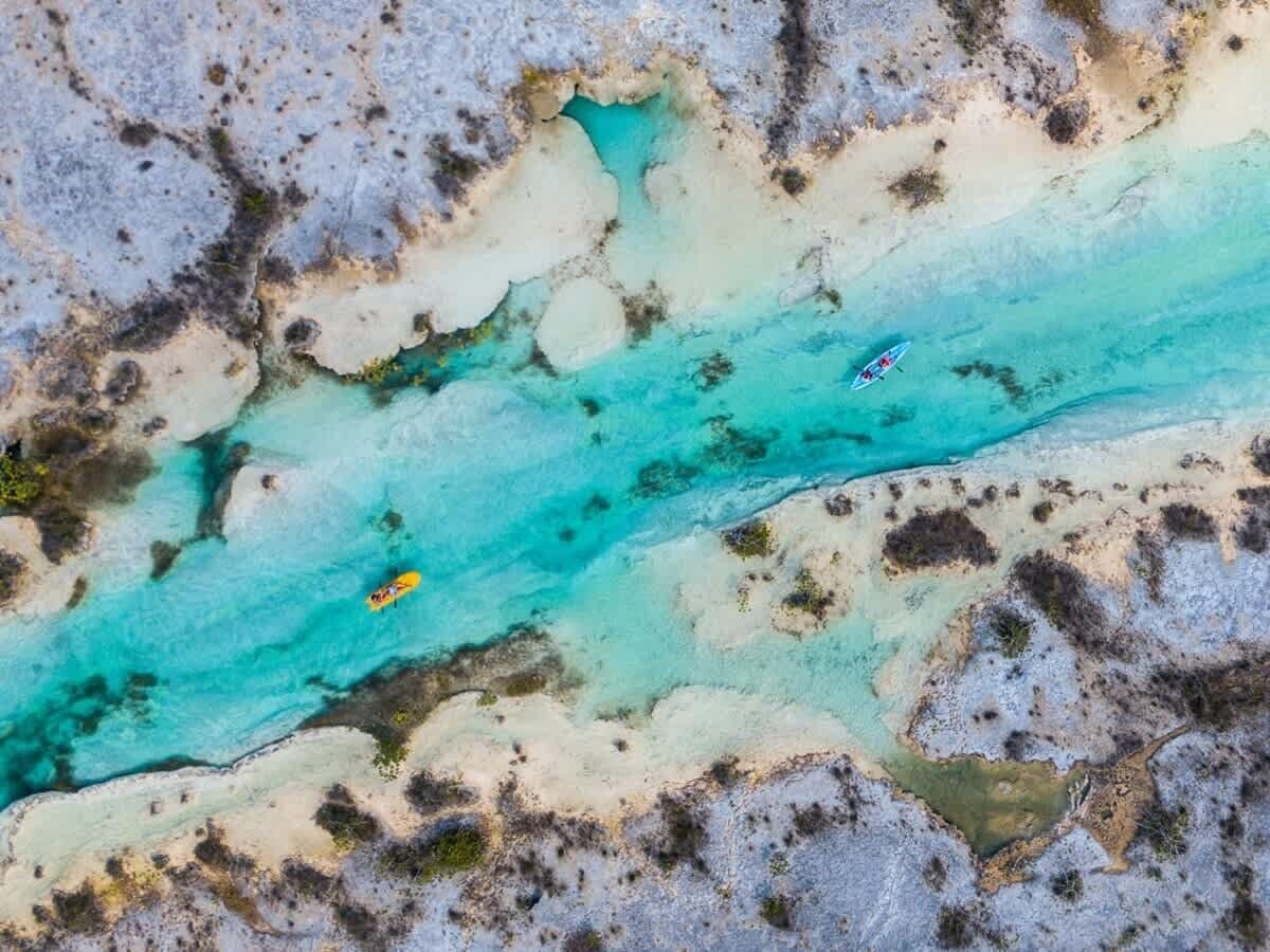 An aerial view of a turquoise river with kayaks.