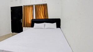 A single bed with white bedding in a room with a black wardrobe and curtains. - OYO Life 92754 Kost Griya Perdana (Mataram)