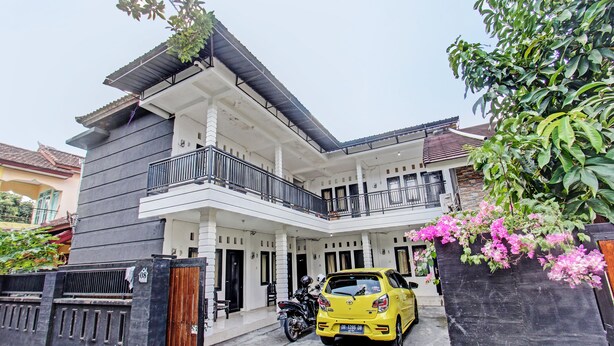 A two-story house with a balcony, a motorcycle parked in front, and a yellow car parked in the driveway. - OYO Life 92754 Kost Griya Perdana (Mataram)