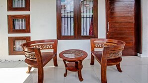 A wooden table and two chairs with intricate carvings, positioned in front of a building with multiple windows and a wooden door. - OYO Life 92754 Kost Griya Perdana (Mataram)