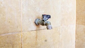 A bathroom with beige tiles and a visible water spigot. - OYO Life 92754 Kost Griya Perdana (Mataram)