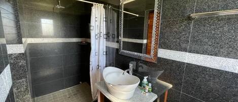 Un baño con un lavamanos grande y blanco, un espejo con marco decorativo y una zona de ducha.
