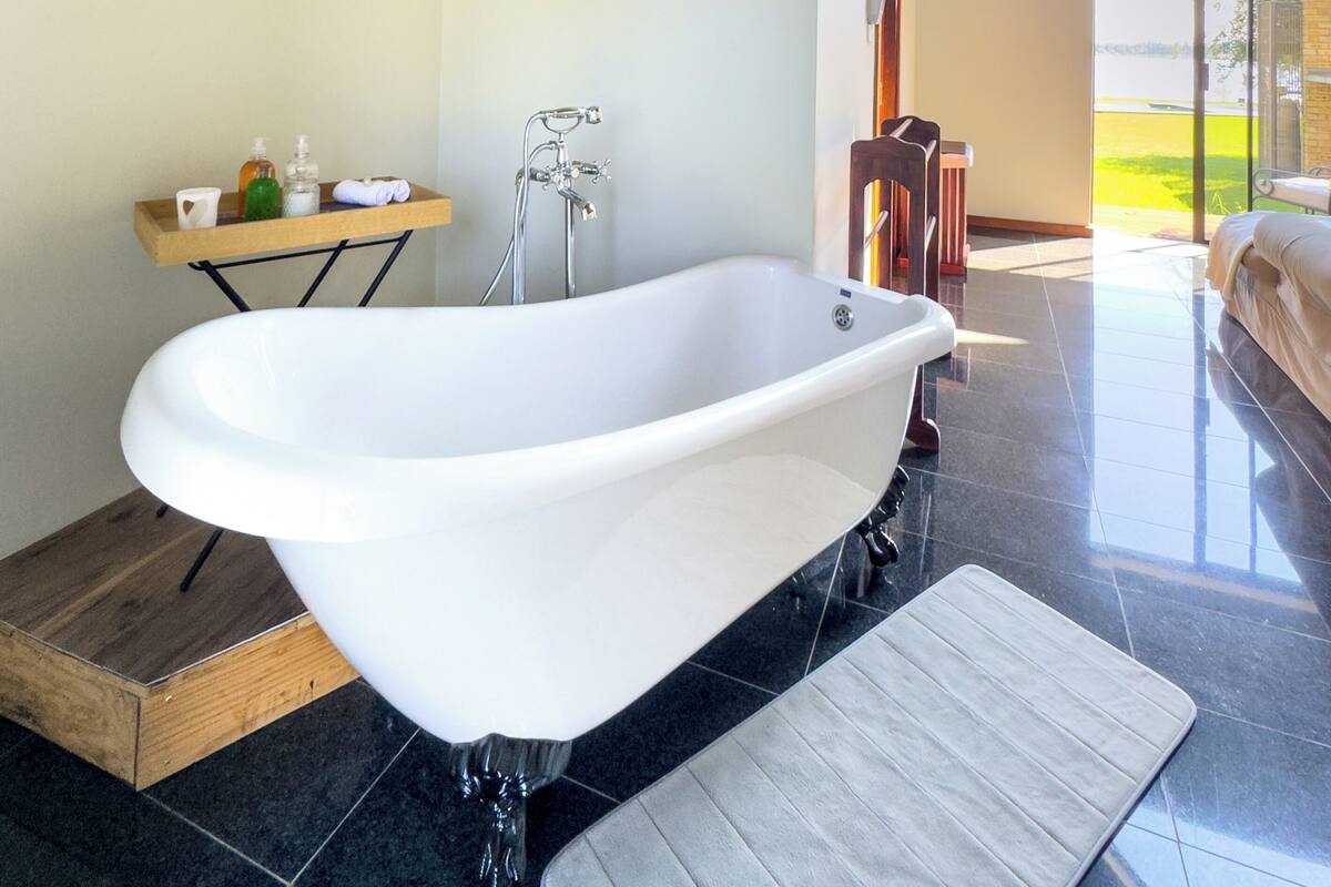A modern bathroom with a freestanding bathtub, a wooden vanity, and a large window offering a view of the outdoors.