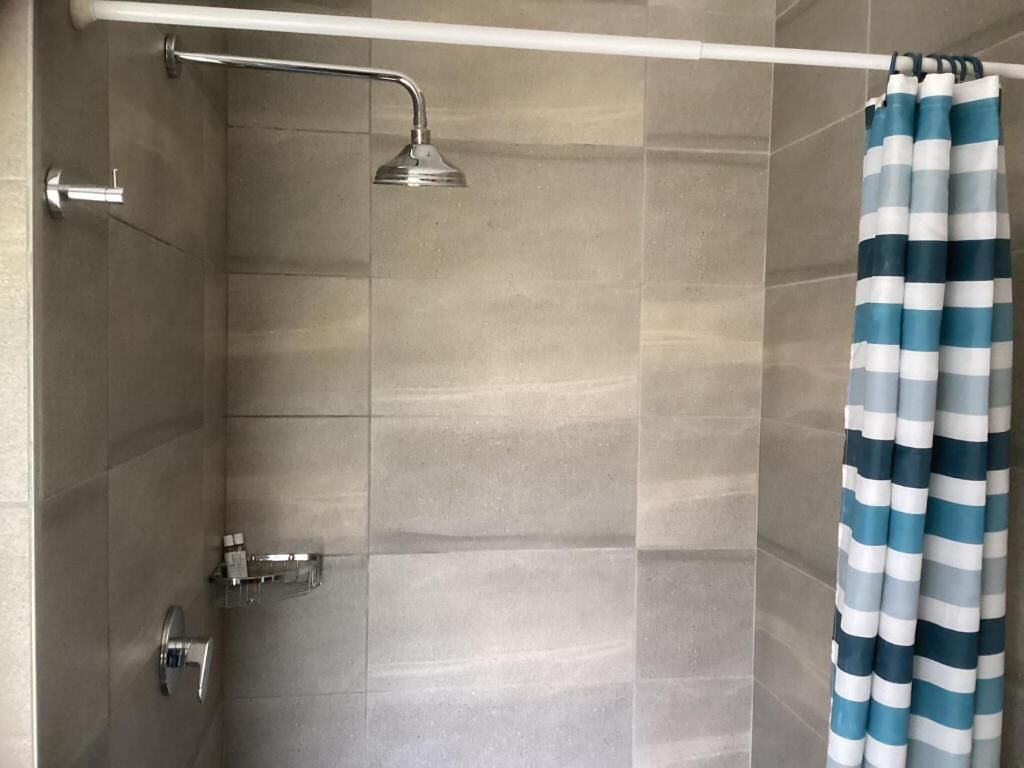 A shower with a handheld showerhead, a towel rack, and a striped shower curtain.