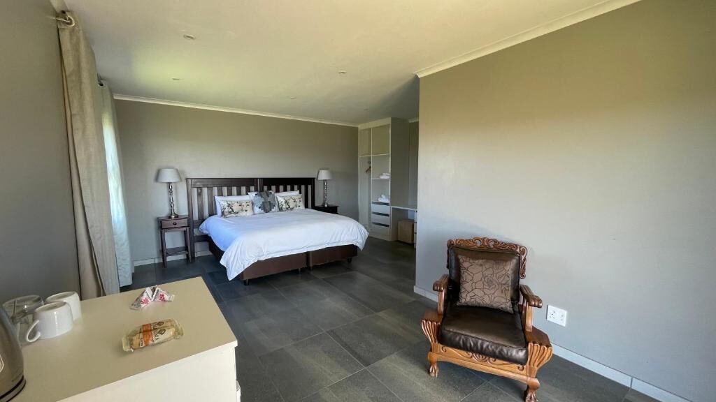 A hotel room with a bed, a chair, a desk with a lamp, and a wardrobe.