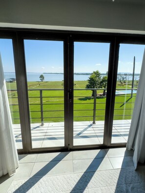 A balcony with a view of a grassy area, a body of water, and distant land. - The Vaal Guesthouse (Metsimaholo)