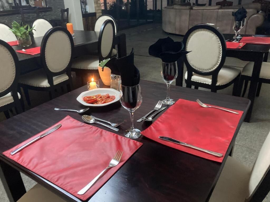 A dining table set with red placemats, silverware, and a candle.