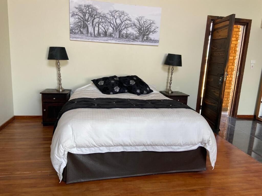 A neatly made bed with a white and black bedspread, flanked by two bedside tables with lamps, a framed picture on the wall, and a wooden door.
