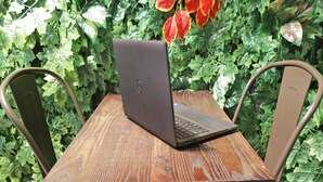 A laptop on a wooden table with metal chairs, surrounded by green foliage. - OYO Life 92925 Kost Bu Mala 2 Syariah (Sukorejo)