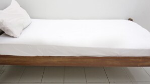 A single bed with a wooden frame and white bedding in a room with white walls and tiled flooring. - OYO Life 92925 Kost Bu Mala 2 Syariah (Sukorejo)