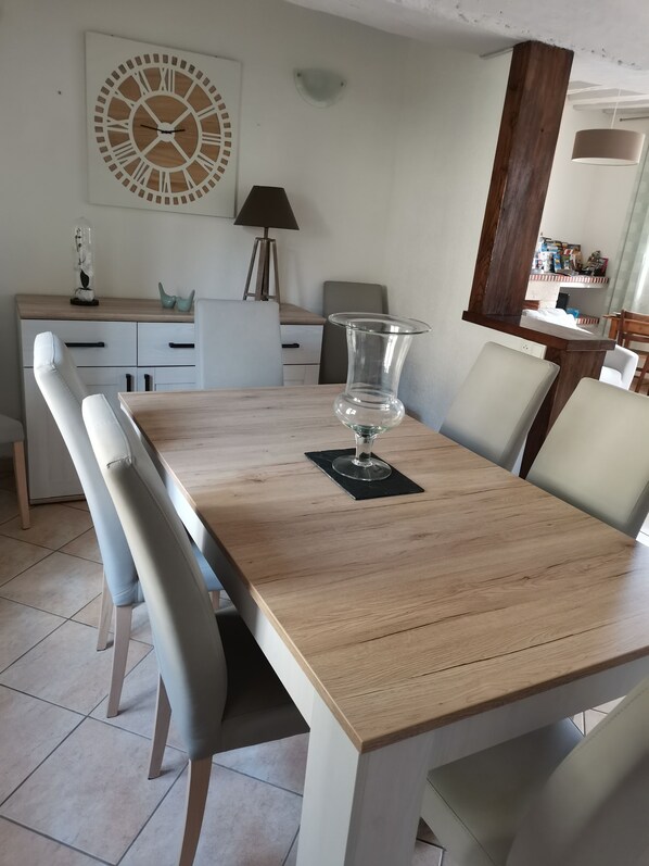 A dining area with a wooden table, white chairs, a wall clock, and a lamp.