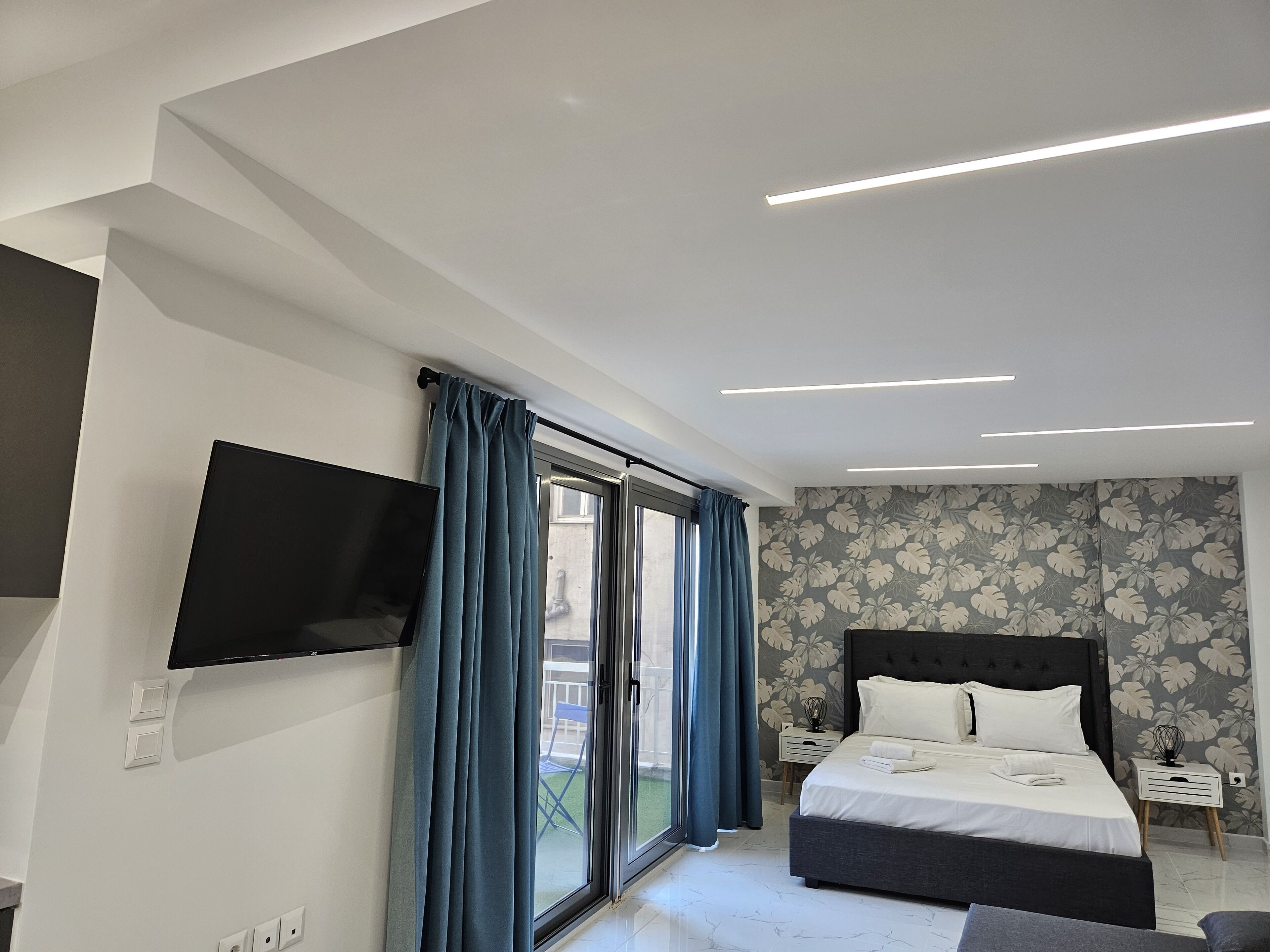 A modern bedroom with a bed, a TV mounted on the wall, and a sliding glass door leading to an outdoor area.