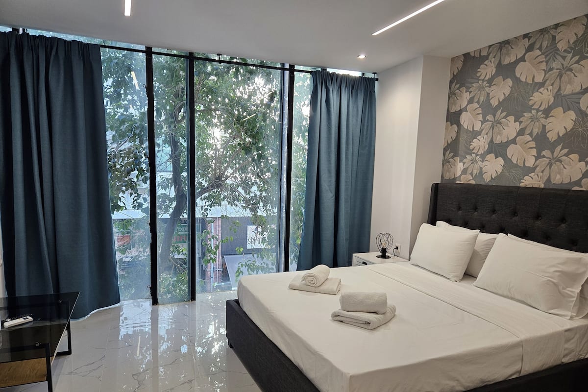 Um quarto moderno com uma cama grande, uma mesinha de cabeceira e vista através de janelas do chão ao teto.