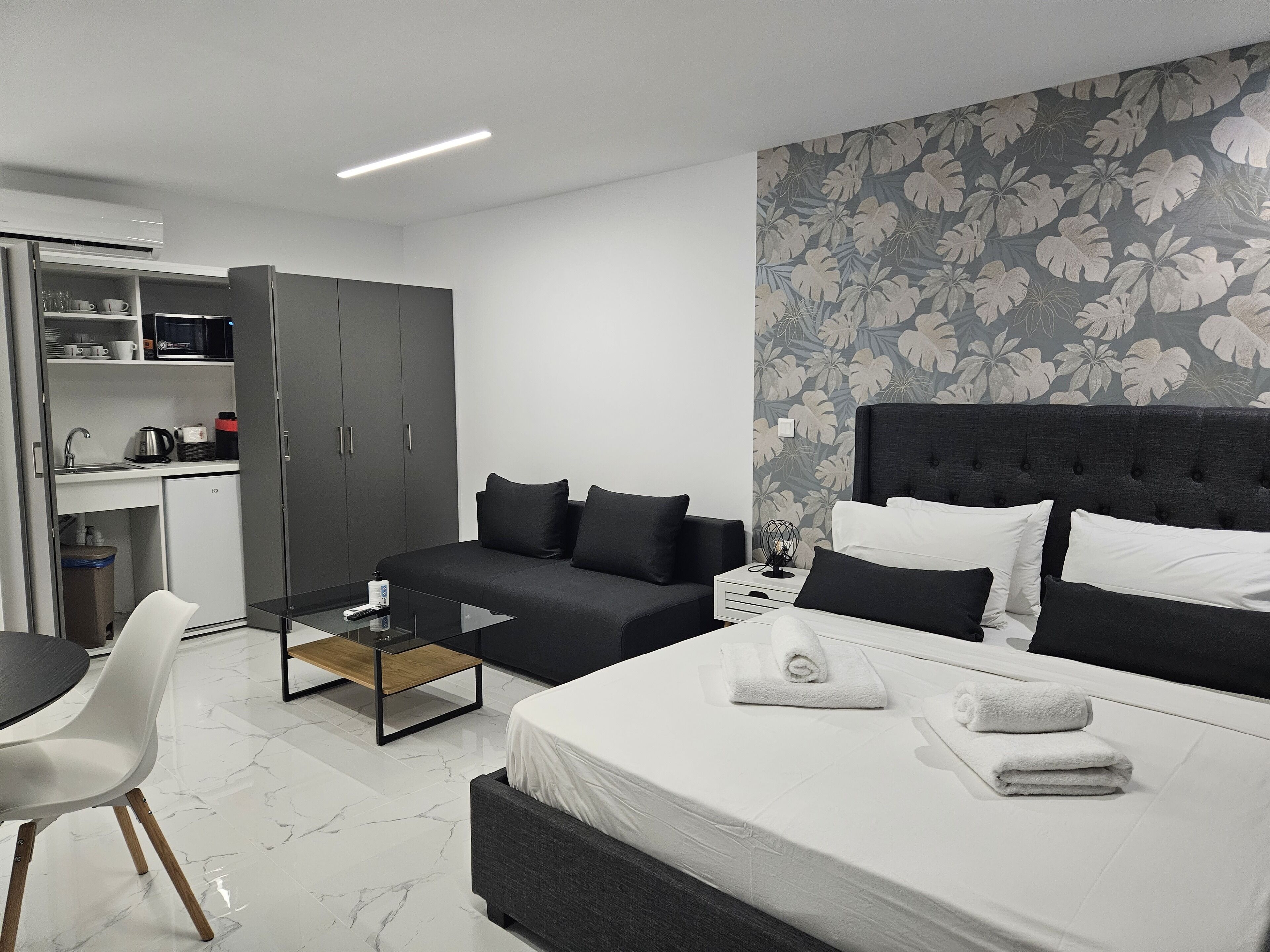 A modern hotel room with a bed, a sofa, a small table, a desk, and a kitchenette.