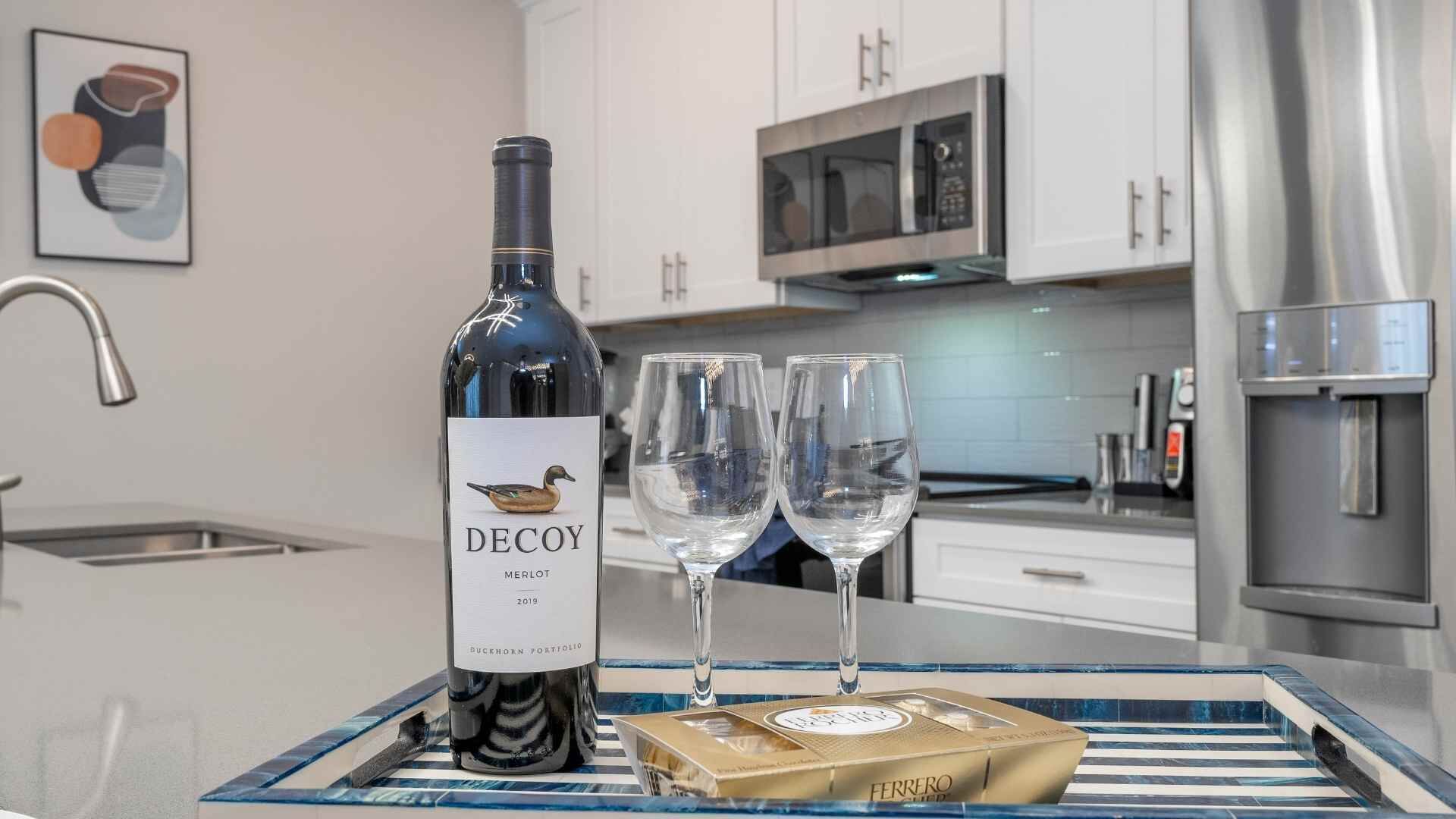 Eine Flasche Decoy Merlot 2019, zwei leere Weingläser und eine Ferrero-Schokolade auf einem Tablett in einer modernen Küche mit weißen Schränken und Edelstahlgeräten.