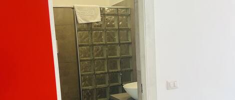 A bathroom with a glass shower enclosure, a white sink, and a red accent wall.