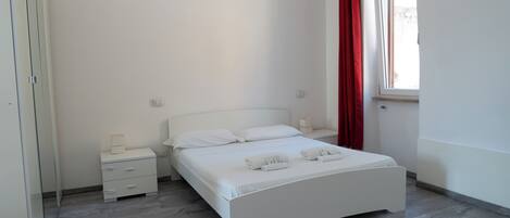 Un dormitorio con cama, mesitas de noche y ventana con cortinas rojas.