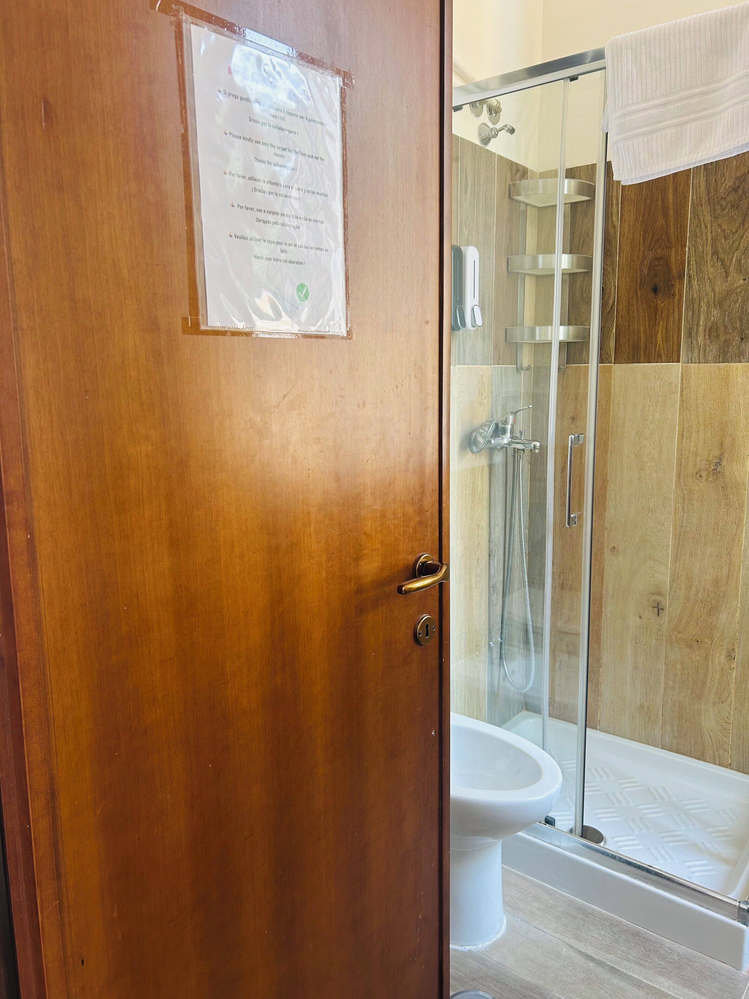 A wooden door with a notice, a glass shower enclosure, a white bathtub, and a toilet.