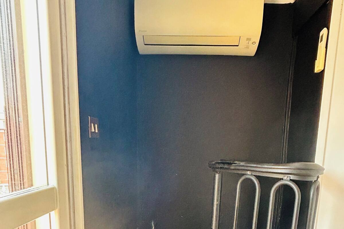 A room with a window, a trash bin, and a wall-mounted air conditioner.