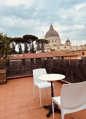 Una terraza con sillas y una mesa blancas, con vista a un edificio histórico con cúpula.