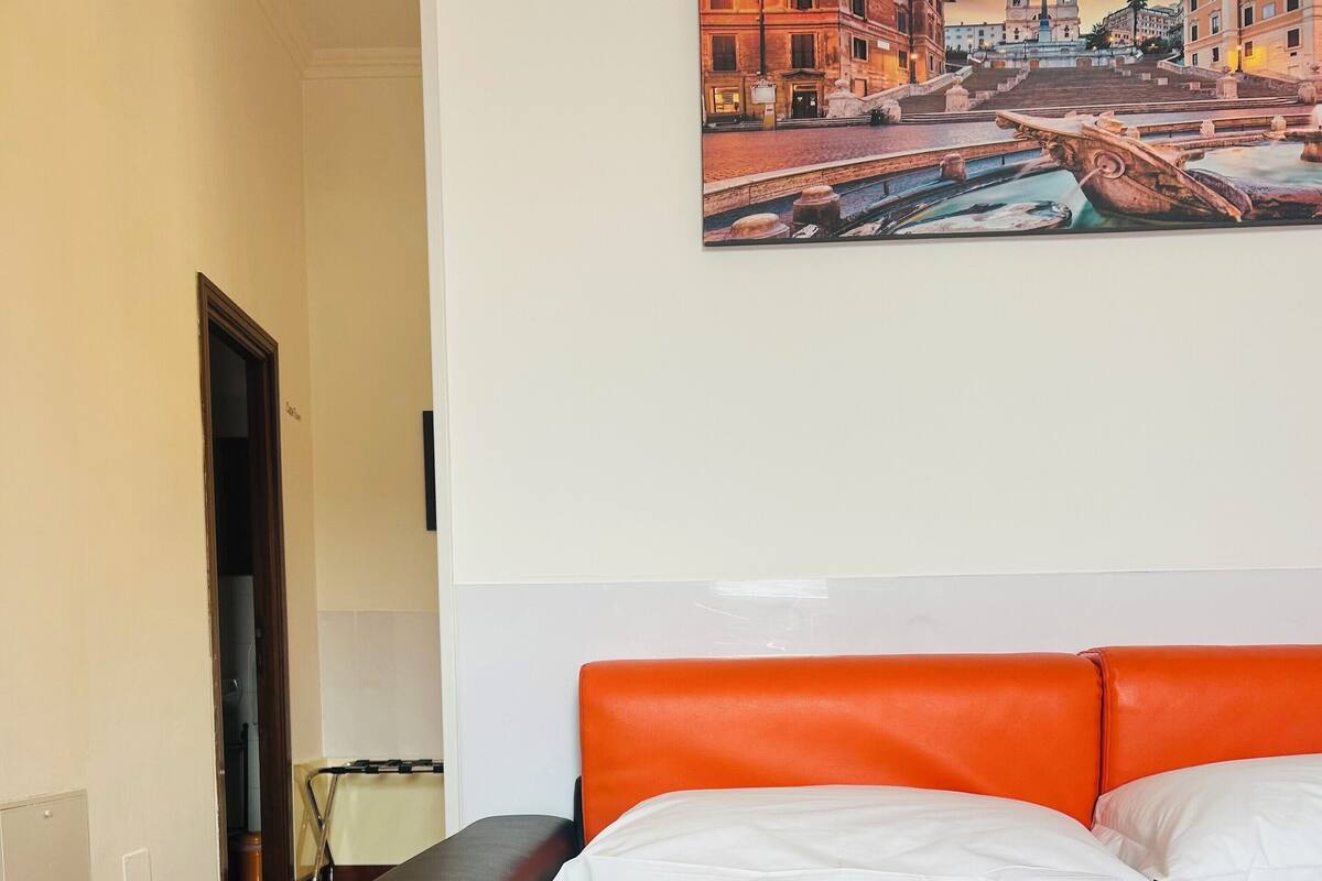A hotel room with a bed, a black suitcase, and a painting of a cityscape on the wall.