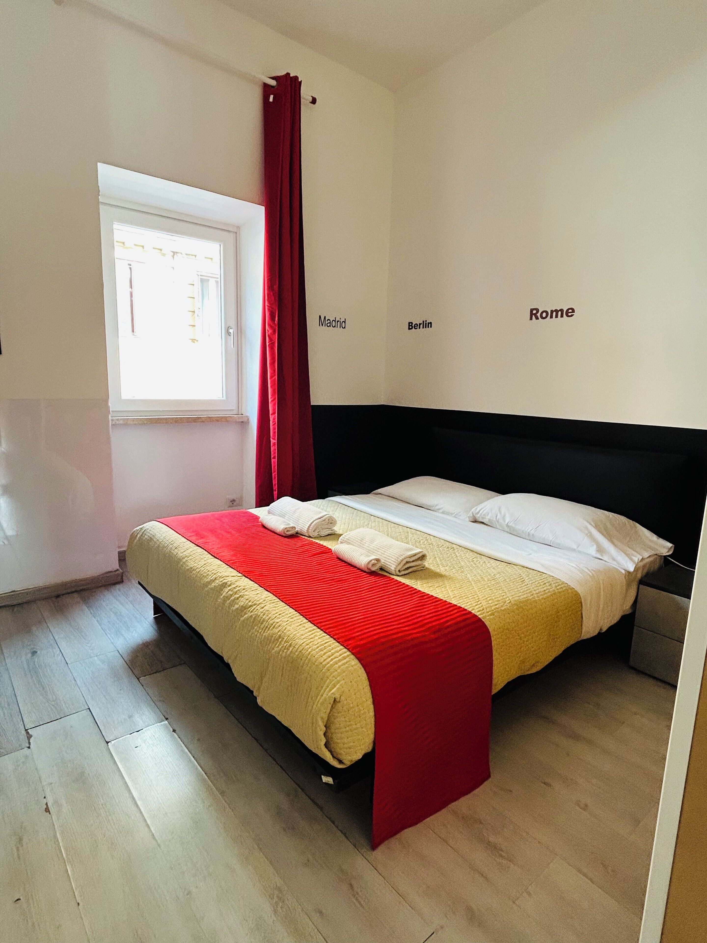 A bedroom with a bed, a window with curtains, and a wall with city names.