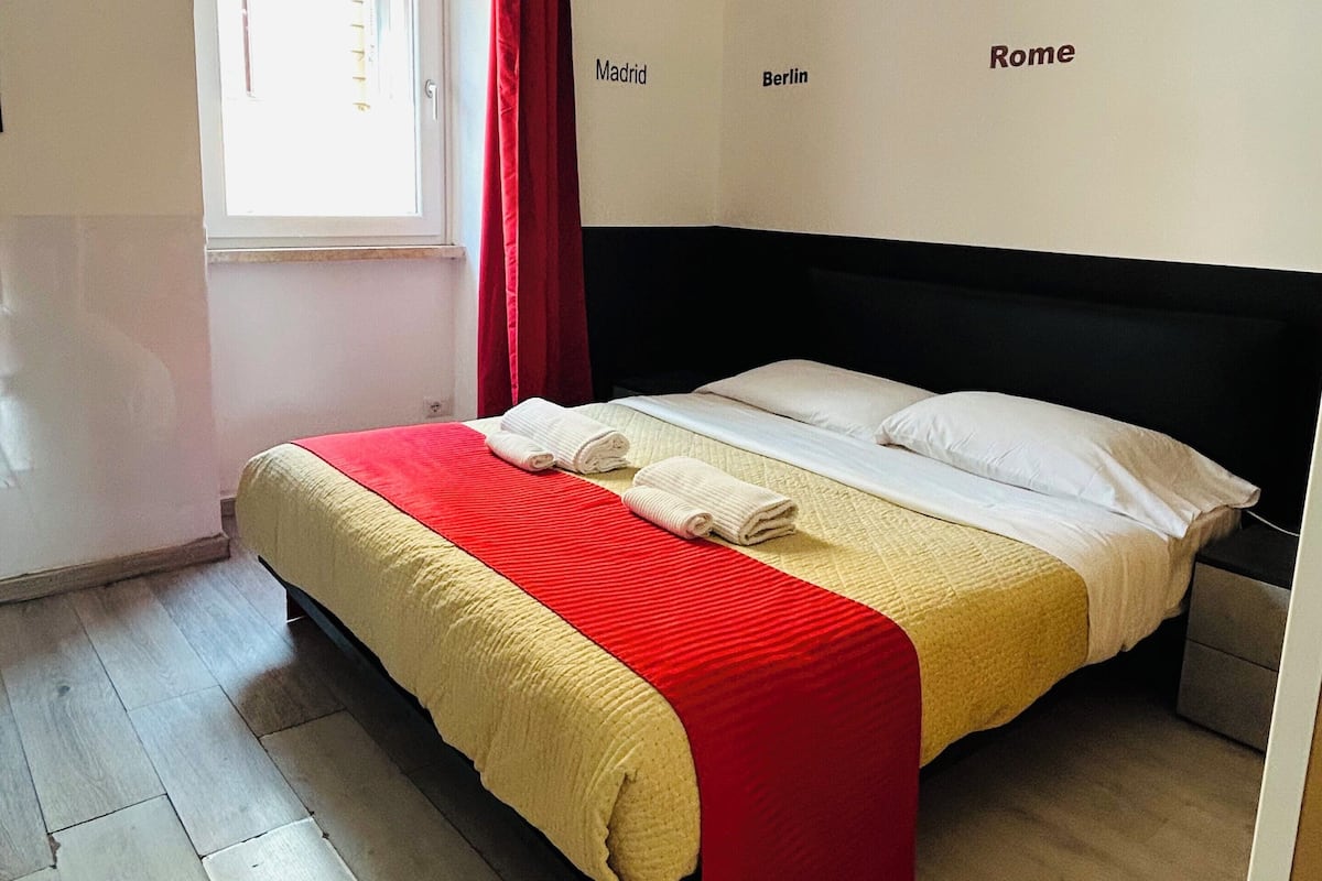 A bedroom with a bed, a window with curtains, and a wall with city names.