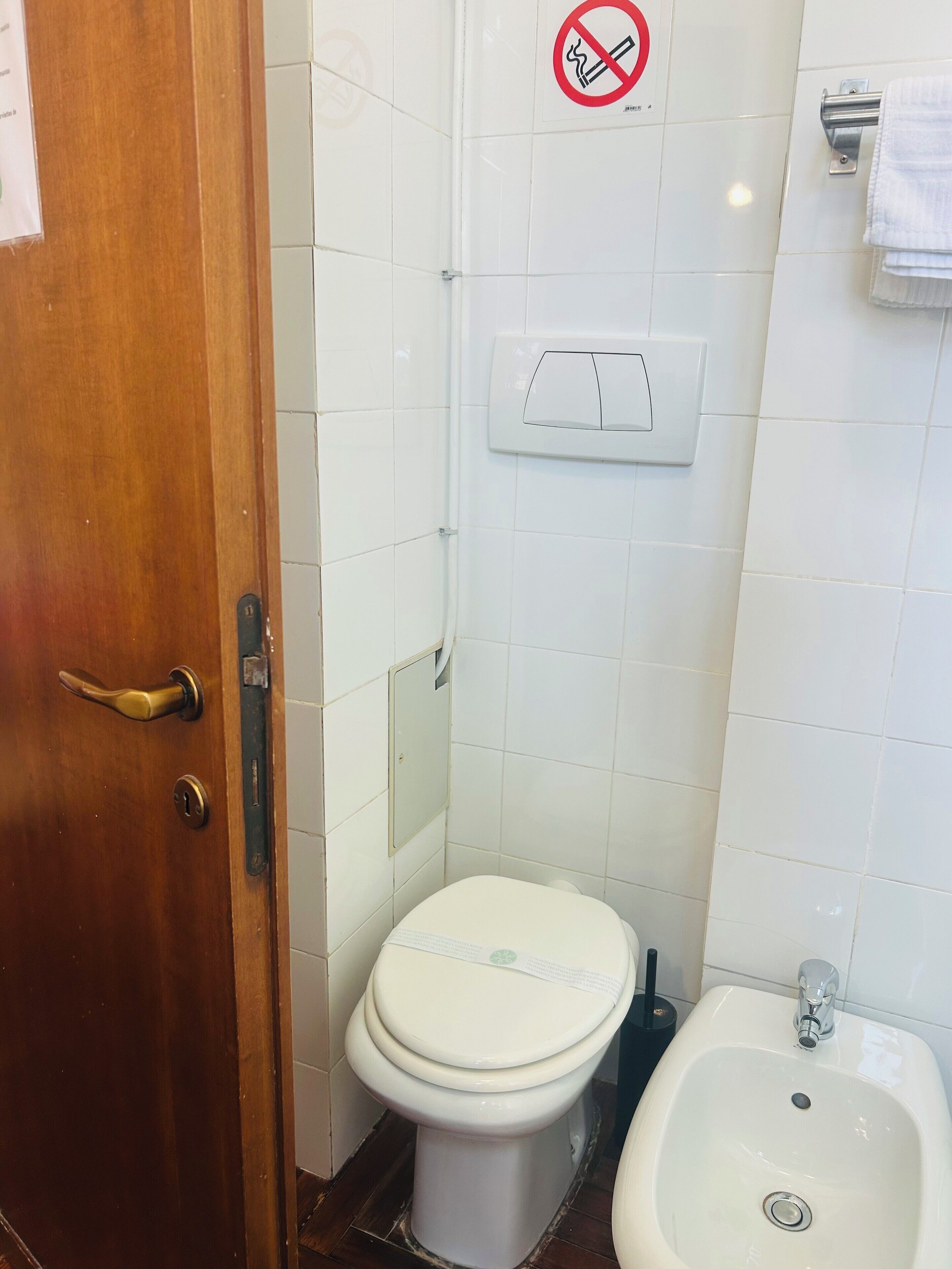 Un baño pequeño y limpio con inodoro, bidé y un cartel de prohibido fumar en la pared.