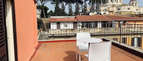 A balcony with a white table and chairs, overlooking a cityscape with historic buildings and a large dome.