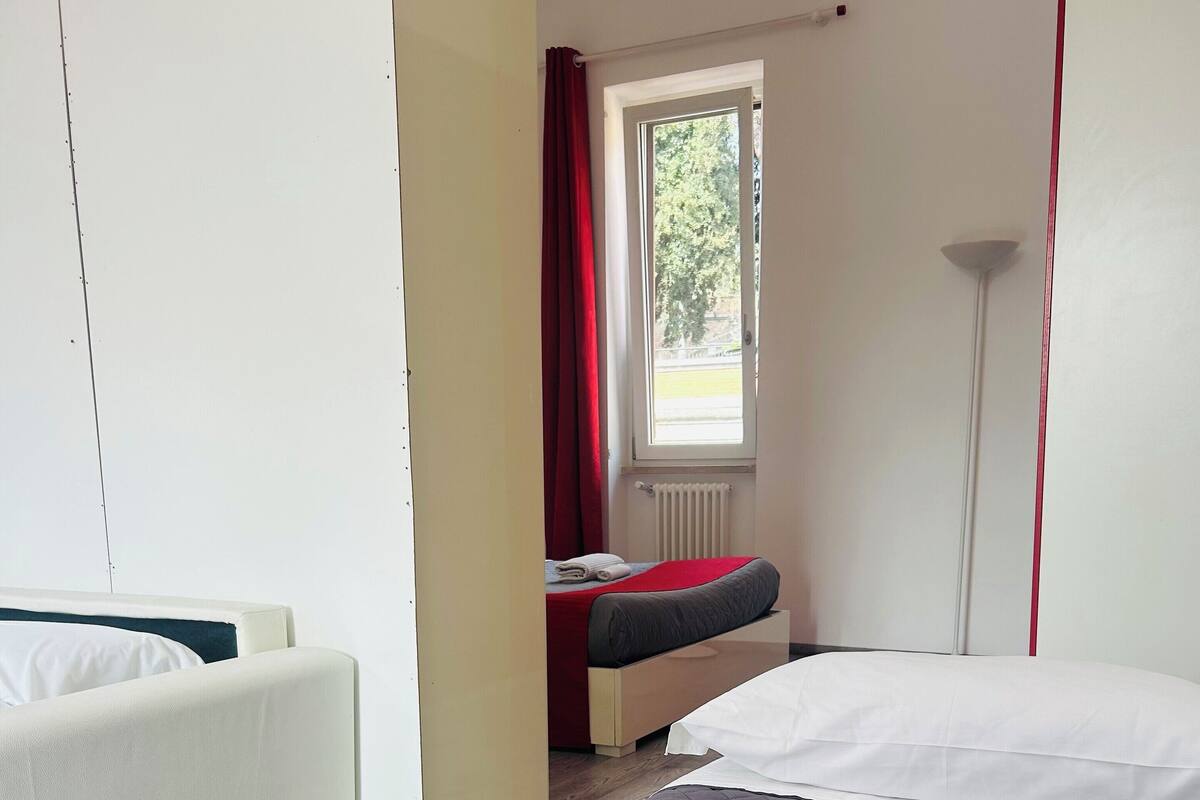 A modern hotel room with a large bed, a sofa, and a window with red curtains.
