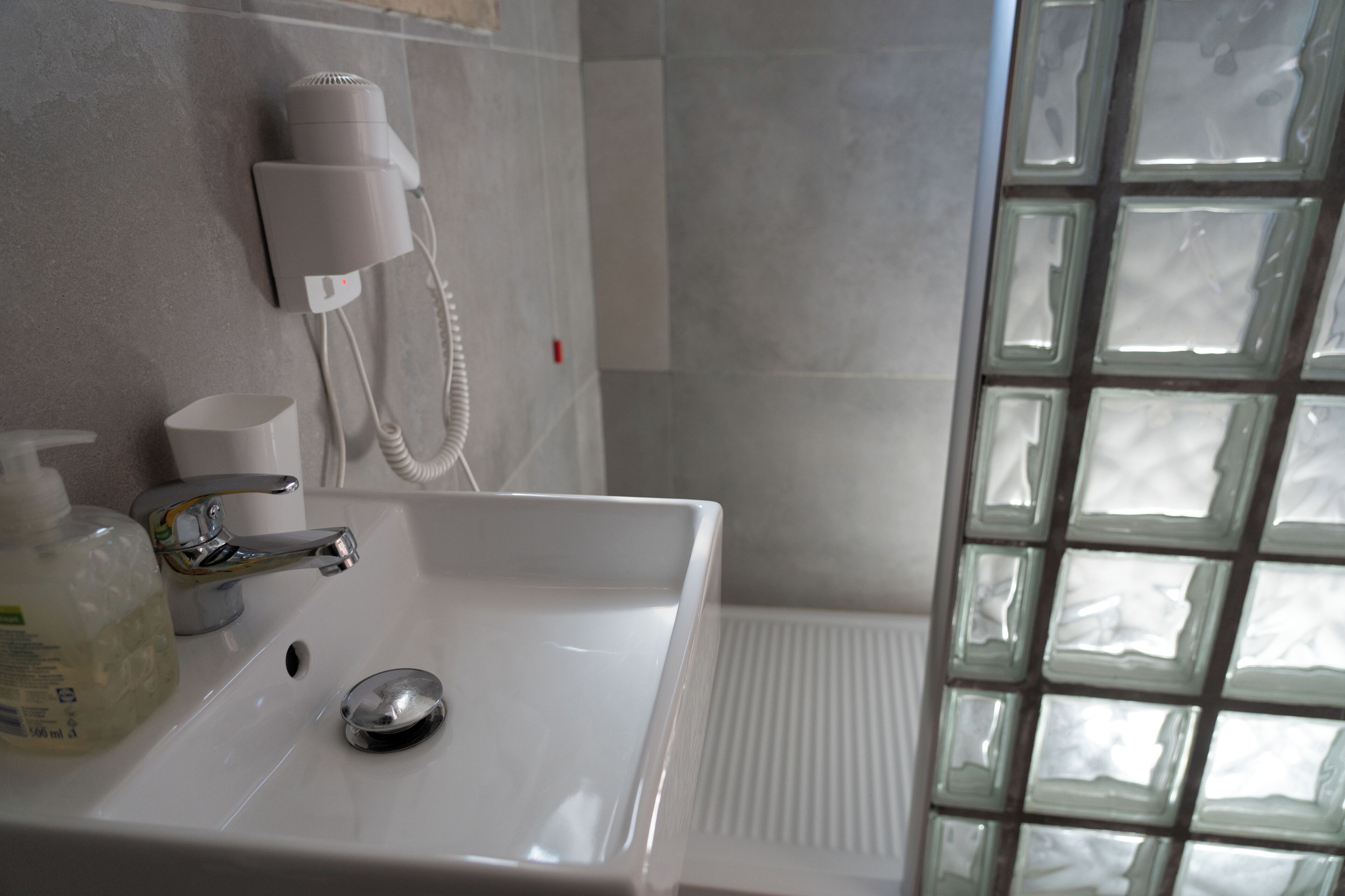 A bathroom with a white sink, a hairdryer, and a bottle of shampoo.