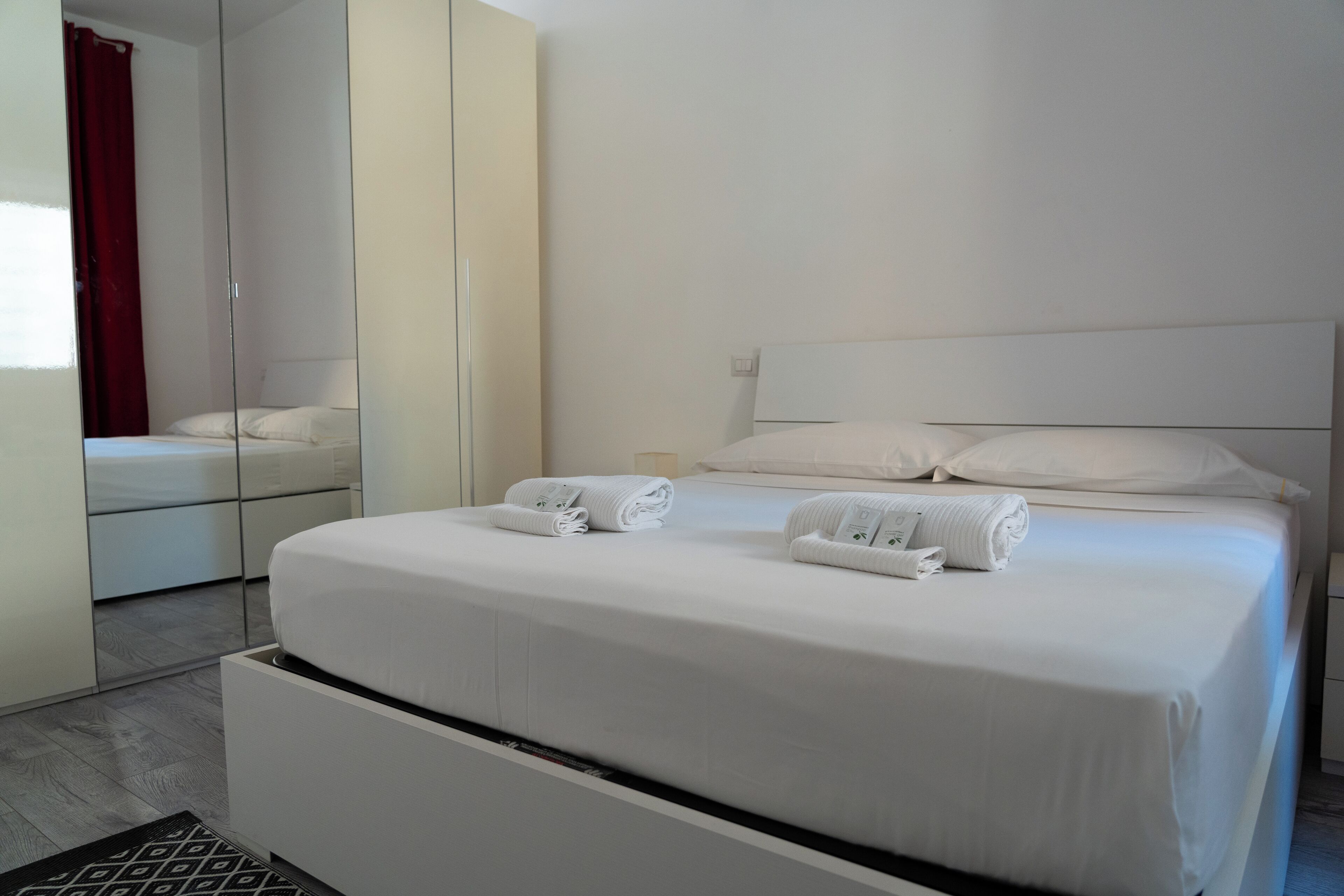A modern hotel room with a large bed, a mirror, and a wardrobe.