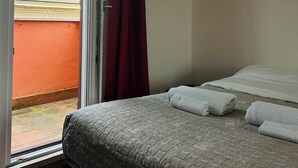 Un dormitori amb un llit, una finestra que dona a un edifici i una cortina vermella.