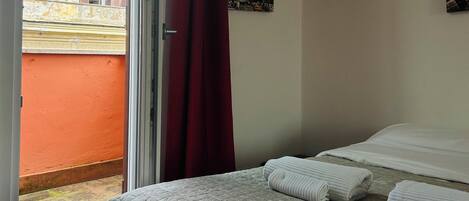 A bedroom with a bed, a window with a view of a building, and a red curtain.